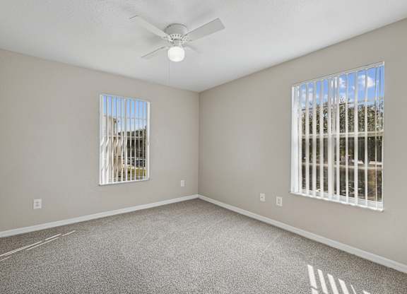 A room with a ceiling fan and two windows.