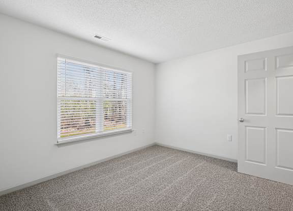 A room with a white door, carpeted floor, and a window with blinds.