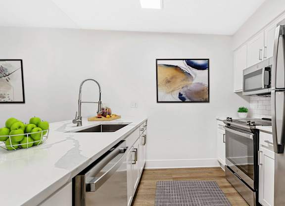 A modern kitchen with a white countertop and stainless steel appliances. at Woodlyn on the Green Apartment Homes, Cary, 27513