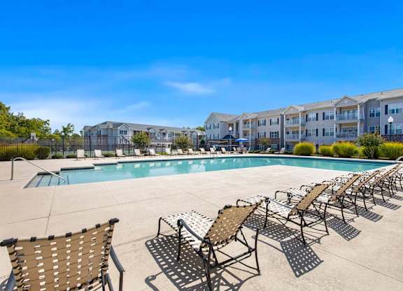 A pool surrounded by sun loungers and chairs with apartment buildings in the background at Ethan Pointe Apartments, North Carolina, 27215