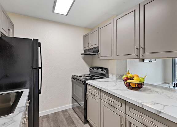 Kitchen with Grey Cabintery, Plank Flooring, and Efficient Appliances, Providing View into Spacious Living Area at Campo Basso Apartment Homes, Lynnwood, 98087