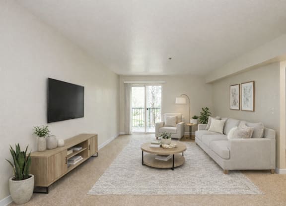 A living room with a white couch, a coffee table, and a flat-screen TV mounted on the wall.