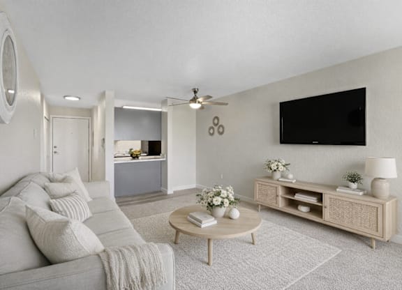 A living room with a grey couch, a wooden coffee table, and a flat screen TV mounted on the wall.