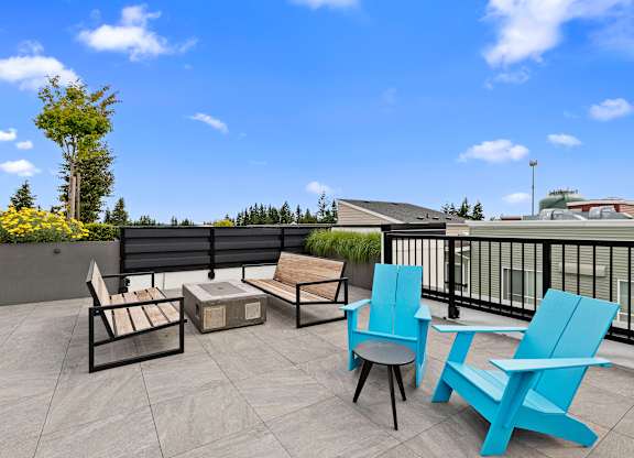 Two Blue Adirondack Chairs with two wooden benches facing cozy fireplace on the Resident Rooftop Lounge with a blue sky in the background at Arabella Apartment Homes, Shoreline, Washington 98155