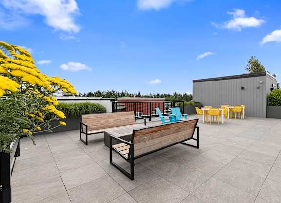 a roof terrace with a benches facing the cozy firepit with chairs and yellow flowers at Arabella Apartment Homes, WA 98155