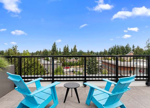 a pair of blue Adirondack chairs in the rooftop lounge area overlooking the view with a table and stool at Arabella Apartment Homes, WA 98155