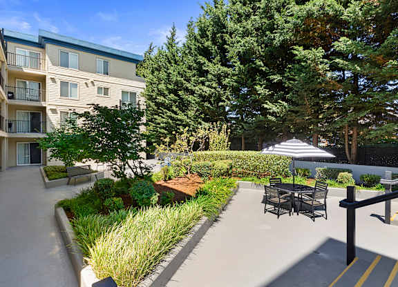 a courtyard with shaded area and a table and chairs with an umbrella at Guinevere Apartment Homes, Washington