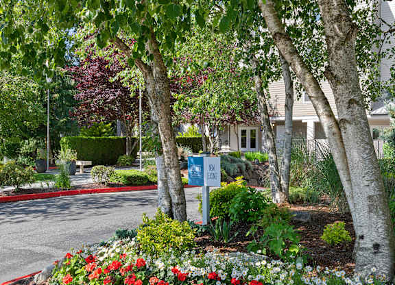 Entrance with trees and flowers in front of property building at West Mall Place Apartment Homes, Everett, WA