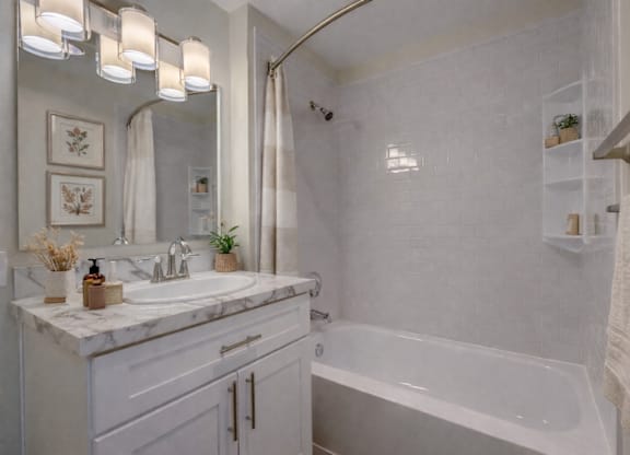 A white bathroom with a marble countertop and a white bathtub.