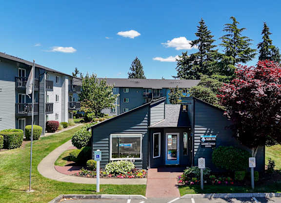 A small building with a blue door is surrounded by greenery and other buildings.