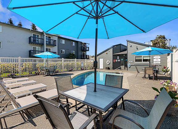 a patio with a pool and chairs and umbrellas at Pacific Park Apartment Homes, WA 98026