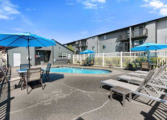 a patio with a pool and chairs and umbrellas at Pacific Park Apartment Homes, Washington