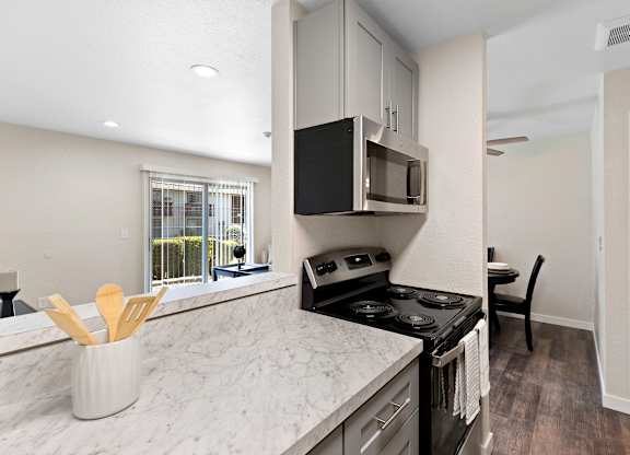 Cozhy Kitchen with Stainless Steel Appliances, Plank Flooring, Spacious Cabinetry, and View of the Living Area at Pinewood Square Apartment Homes, Lynnwood, WA