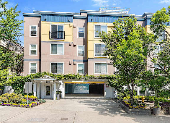 an apartment building with a driveway and trees in front of it at Sir Gallahad Apartment Homes, Bellevue, WA
