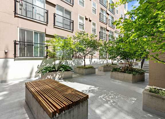 a courtyard with a wooden bench and trees in front of  Sir Gallahad Apartment Homes, Washington, 98004