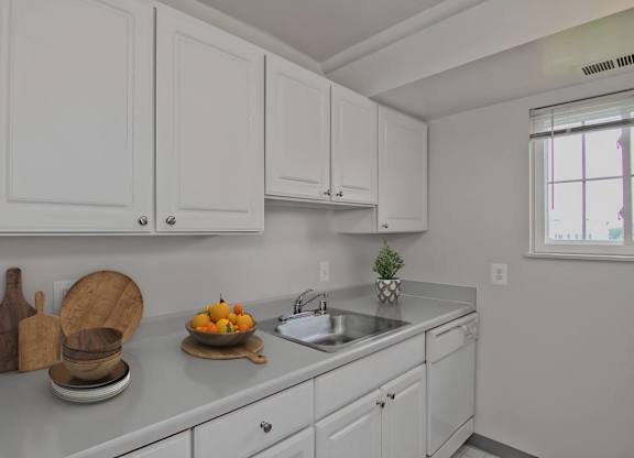 A kitchen with white cabinets and a countertop with a bowl of fruit on it.