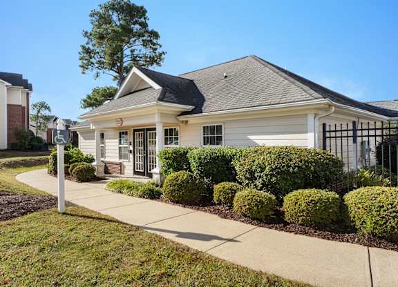 A small white house with a black roof and a sign with a wheelchair symbol in front of it. at Village on the Lake Apartments, North Carolina, 28390