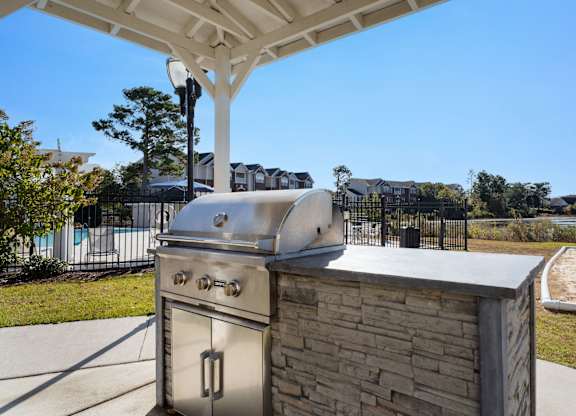 A stainless steel grill is attached to a brick wall under a white canopy at Village on the Lake Apartments, North Carolina, 28390