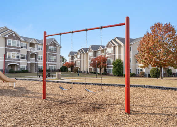 A playground with a red swing set in front of apartment buildings. at Stone Gate Apartments, Apartments, Spring Lake, NC