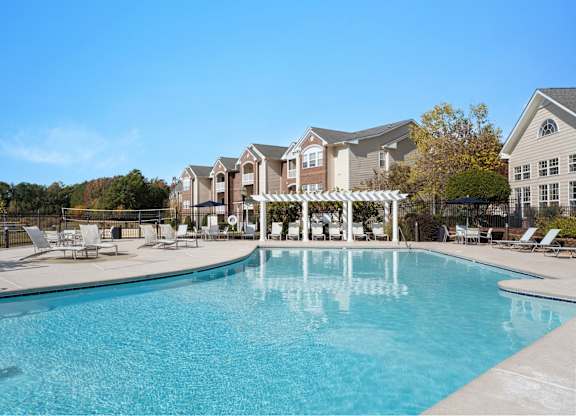 A large swimming pool in front of a building with a white pergola. at Village on the Lake Apartments, North Carolina