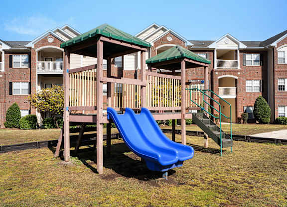 A playground with a blue slide in front of apartment buildings at Village on the Lake Apartments, North Carolina