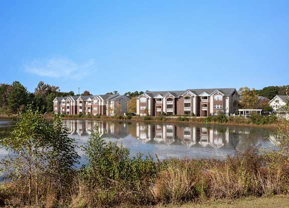 A row of houses are reflected in the water. at Village on the Lake Apartments, Spring Lake, 28390