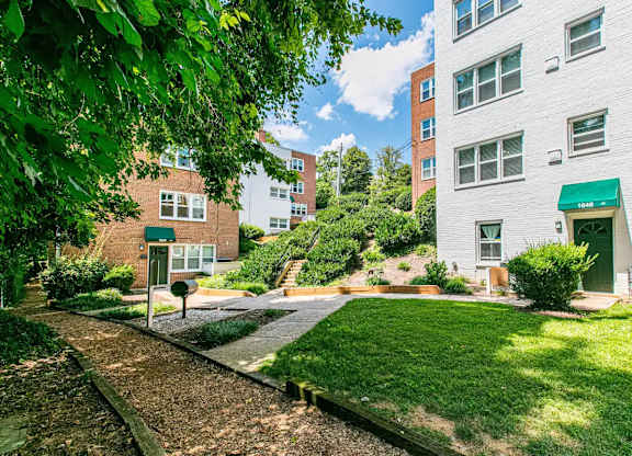 A white building with a green awning sits next to a grassy area. at Park Georgetown Apartments, Arlington, VA 22209