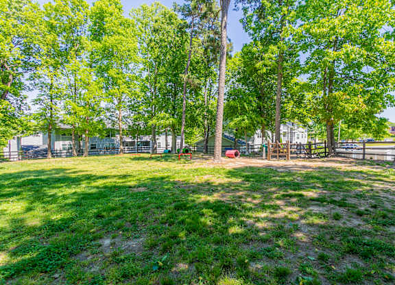 A grassy area with trees and a fence in the background at West Pointe Apartments, Burlington, North Carolina