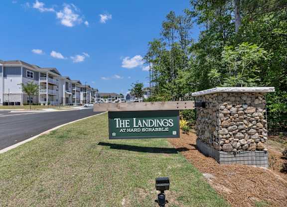 A sign for The Landings at Hard Scrabble is in front of a stone wall.
