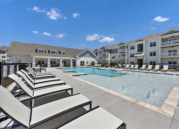 A pool area with sun loungers and apartment buildings in the background.
