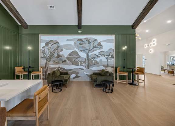 A room with a large mural of a tree on the wall and several chairs and tables scattered around.