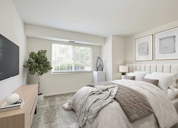 A bedroom with a large bed, a desk with a keyboard, and a plant at Fairfax Square Apartments, Fairfax, VA, 22031