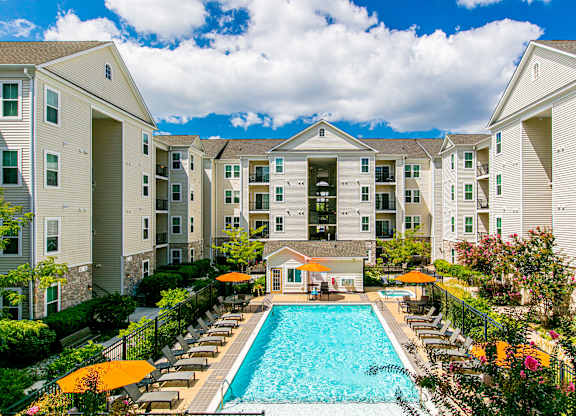 A large swimming pool surrounded by lounge chairs and umbrellas in front of apartment buildings. at Kensington Place Apartments, Virginia