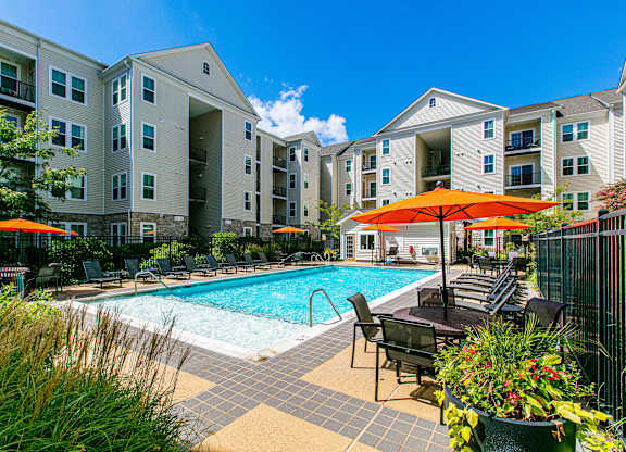 A pool area with chairs and umbrellas in front of a building. at Kensington Place Apartments, Woodbridge, VA