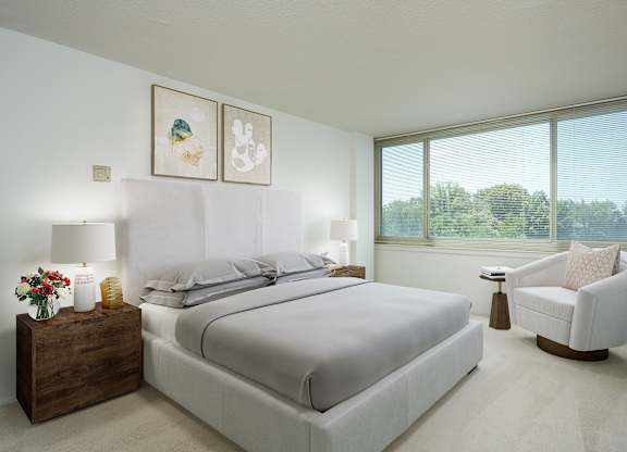 A bedroom with a large bed, a chair, and a window overlooking trees.