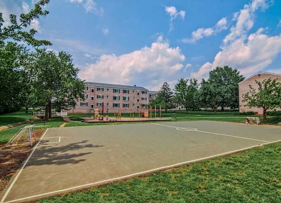 A basketball court is surrounded by grass and trees in front of a building at Dulles Glen Apartments, Herndon, Virginia