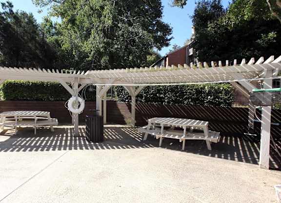 A white pergola with a bench underneath it.