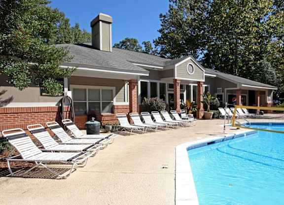 A poolside scene with a house and lounge chairs.