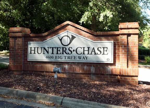 A brick sign that says Hunters Chase stands in front of a tree.