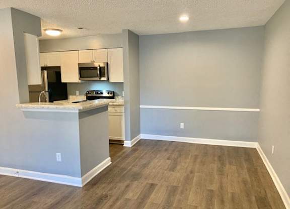 A kitchen with a black refrigerator, white cabinets, and a wooden floor.