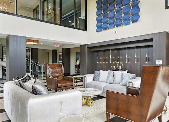 A modern living room with a white couch, a brown leather chair, and a blue abstract painting on the wall at Alinea Town and Country Luxury Apartments in Des Peres MO 63131..