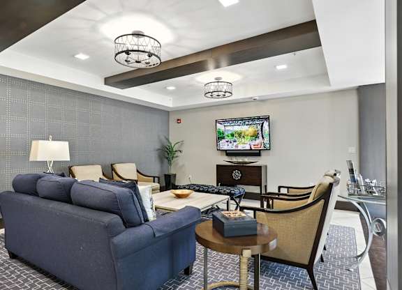 A living room with a blue couch, a chair, a coffee table, and a television at Alinea Town and Country Luxury Apartments in Des Peres MO 63131..