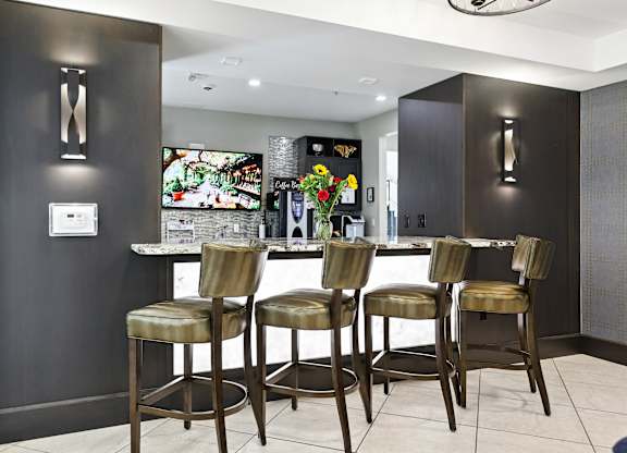 A bar area with three stools and a television in the background at Alinea Town and Country Luxury Apartments in Des Peres MO 63131.