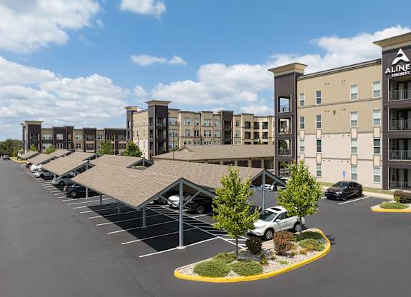 A parking lot in front of a building with the sign Alinea on it and carports at Alinea Town and Country Luxury Apartments in Des Peres MO 63131..