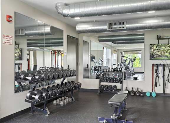 A gym with a variety of equipment including dumbbells, weight plates, and a bench press at Alinea Town and Country Luxury Apartments in Des Peres MO 63131.