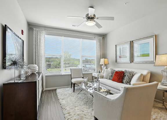 A living room with a white couch, a coffee table, and a ceiling fan at Alinea Town and Country Luxury Apartments in Des Peres MO 63131.