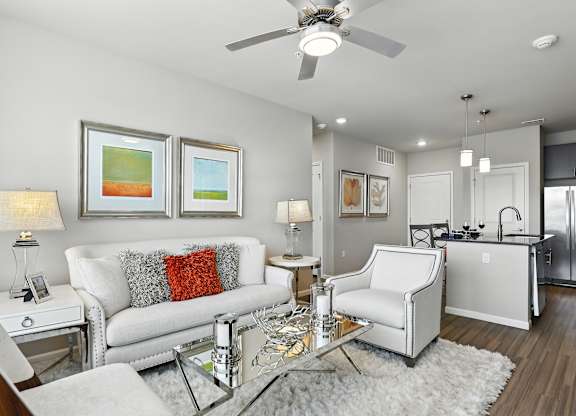 A modern living room with a white sofa, a glass coffee table, and a ceiling fan at Alinea Town and Country Luxury Apartments in Des Peres MO 63131.