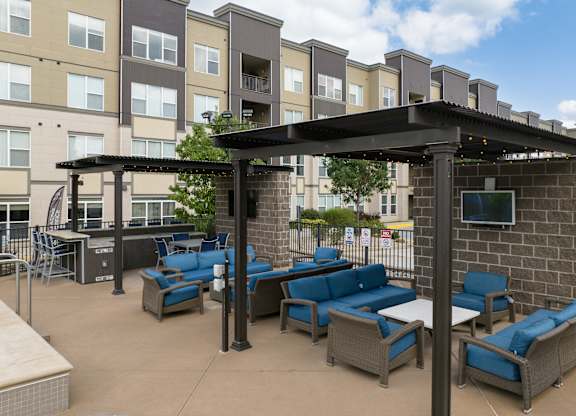 A patio with blue cushioned furniture and a black pergola at Alinea Town and Country Luxury Apartments in Des Peres MO 63131..
