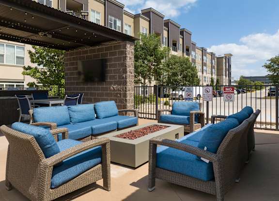A patio with blue cushioned furniture and a brick fireplace at Alinea Town and Country Luxury Apartments in Des Peres MO 63131..