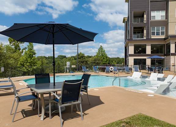 A table with chairs and an umbrella is in front of a poo at Alinea Town and Country Luxury Apartments in Des Peres MO 63131.l.